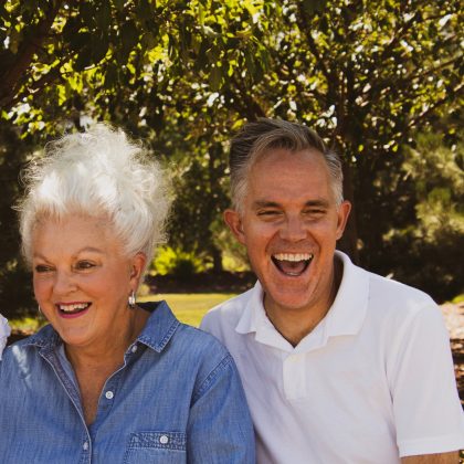 Two elderly patients smile and laugh while standing outside underneath a tree