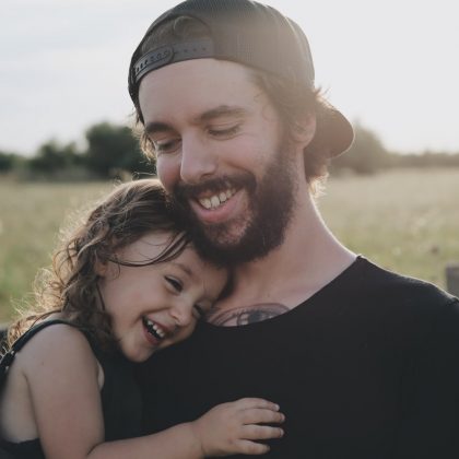 A young father smiles while holding his daughter to his chest