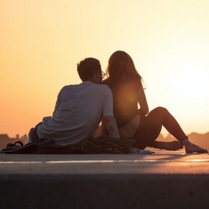 A young couple sit together while watching a sunset