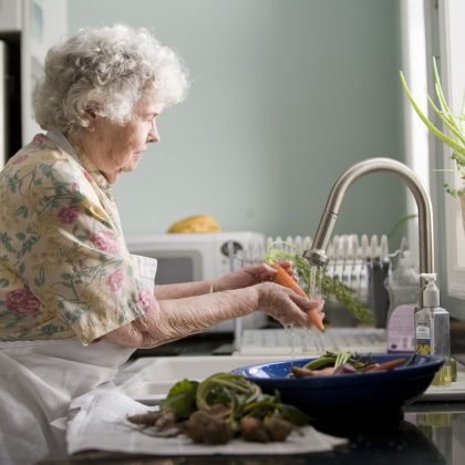 An elderly woman washes a carrot in her kitchen sink