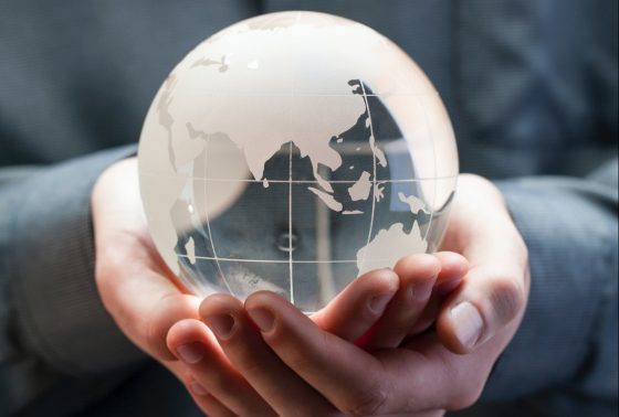 A person holds a glass model of a globe in their hands