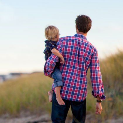 A father holds his son on his hip while taking a walk down a beach