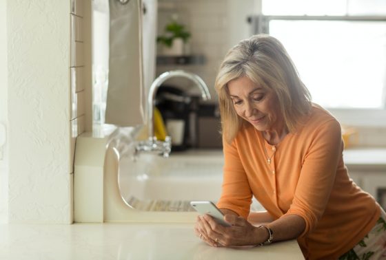 Woman smiling in the kitchen, looking down at her phone
