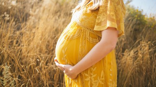 A pregnant mother holds her belly while standing in a field