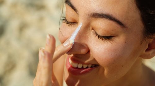 staying sunsmart - woman putting on sunscreen on her nose